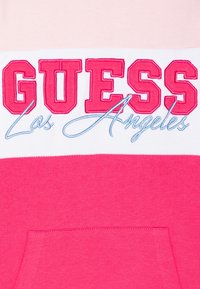 Różowa bluza z kapturem z kontrastującymi jasnoróżowymi paskami. Logo "GUESS" w mocnym różowym haftowaniu, "Los Angeles" w jasnoniebieskim kursywie, kieszeń kangurza.