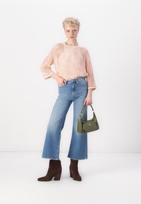 Világos rózsaszín kötött pulóver, kék harangszárú farmer, barna velúr bokacsizma és kis zöld kézitáska; laza fazonú és texturált mintázatú.