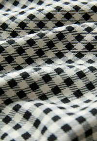 Witte stof met een herhalend patroon van zwarte ruiten en diagonale lijnen, in close-up weergegeven met zachte plooien en detail van de textuur.