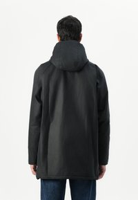 Μαύρο μπουφάν με κουκούλα και λεία, ματ υφή. Διαθέτει πιο μακρύ κόψιμο, ραφές ραγκλάν και μία διακριτική γυαλάδα. Απλός, μινιμαλιστικός σχεδιασμός.