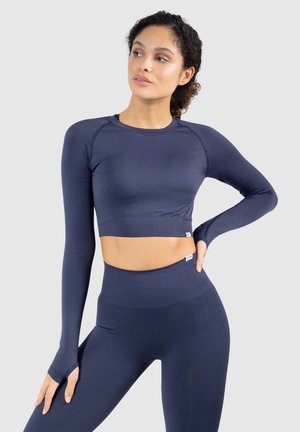 Marineblauwe sportieve crop top met lange mouwen en bijpassende hoge taille legging. Soepele textuur, getailleerd ontwerp en duimopeningaccenten op de mouwen.