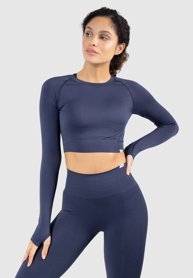 Dunkelblaues, langärmliges, sportliches Crop-Top mit passenden hochgeschnittenen Leggings. Glatte Textur, taillierte Passform und Daumenlöcher an den Ärmeln.