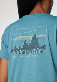 Tiršo v teal barvi z grafiko gore in črnim napisom "Patagonia". Pod zasnovo je napis "REŠITE NAŠ DOMOV PLANET". Lahka tkanina.