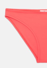 Korall színű bikini alsó, sima, rugalmas anyagból készült. Minimális takarást biztosít, lapos varrásokkal és letisztult, egyszerű dizájnnal rendelkezik.