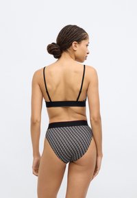 Μαύρο σουτιέν με λεπτές τιράντες, συνδυασμένο με ψηλόμεσο εσώρουχο που έχει επαναλαμβανόμενο σχέδιο λογότυπου σε μαύρο και λευκό, με λεία υφή.