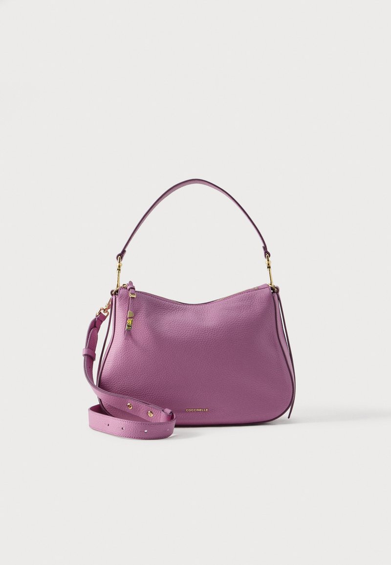 Lilla lærhåndveske med glidelåser i gull, avtakbar skulderstropp og kort håndtak, plassert på hvit bakgrunn.