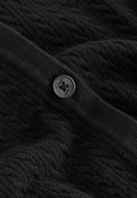 Maglione nero a maglia con motivo a treccia texturizzato e polsini a costine lisce. Presenta un bottone nero con l'iscrizione "Clarks".