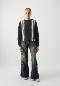 Zwarte gebreide trui met open gatenpatroon en witte strepen, gecombineerd met wijde, vervaagde denim cargos met zijzakken.