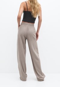 Světle béžové široké kalhoty s elastickým pasem, vyrobené z měkké, splývavé látky; hladký povrch a volný střih od pasu.