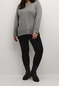 Grå strikket sweater med lange ærmer, ribbet kant og sideåbninger, kombineret med sorte slim-fit bukser og sorte ankelstøvler.