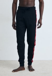 Zwarte sweatpants met een trekkoord in de taille, voorzien van een rode streep langs de zijkanten met logo-accenten, gemaakt van een zachte, gestructureerde stof.