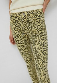 Gula jeans med ett svart tigerstrimmönster, med en klassisk femfickdesign och metallknäppning i midjan.