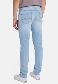 Jeans in denim azzurro chiaro con vestibilità slim, dotati di due tasche posteriori e un sottile dettaglio di cucitura marrone sui bordi delle tasche.