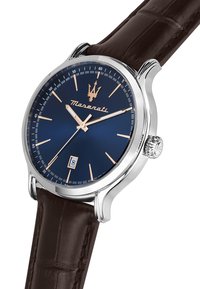 Orologio con cinturino in pelle marrone, cassa in acciaio inox argentato, quadrante blu, indici in tono oro e display della data alle 6. Presenta un dettaglio sulla corona.