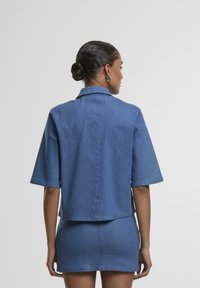 Jachetă din denim cu mâneci scurte, de culoare bleu deschis, cu un croi lejer, asortată cu o fustă mini corespunzătoare. Design curat, fără decorațiuni.