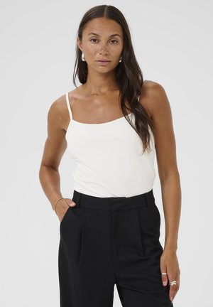 White camisole with thin straps, smooth fabric, and a square neckline paired with high-waisted black trousers featuring front pleats.