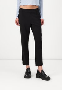 Svarta tapered byxor med en mjuk textur, två framfickor och medelhög midja. Bärs med kraftiga svarta loafers.