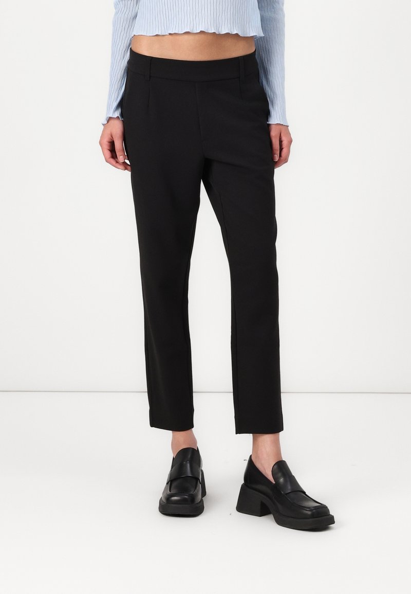 Svarta tapered byxor med en mjuk textur, två framfickor och medelhög midja. Bärs med kraftiga svarta loafers.