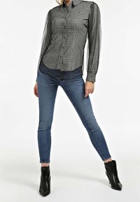 Chemise boutonnée à manches longues en vichy noir et blanc, associée à un jean skinny bleu foncé et des bottines à talons noires.