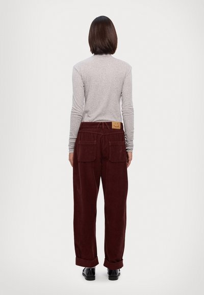 Maroon corduroy pants with a relaxed fit, two back pockets, and a textured finish, paired with a light gray long-sleeve shirt.