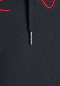 Black hoodie fabric with a textured weave and a red embroidered design. Features a braided drawstring with a silver metal aglet.