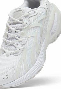 Scarpa da ginnastica bianca con tomaia in rete e dettagli in plastica liscia. Punta arrotondata, suola testurizzata e elementi di design scolpiti distintivi.