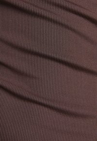Dettaglio ravvicinato di un tessuto marrone a righe verticali, con pieghe morbide che creano ombre e texture sottili.