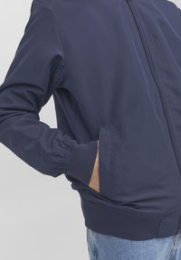 Granatowa bomberka wykonana z gładkiego materiału. Posiada ściągacze przy mankietach, zamek błyskawiczny oraz kieszenie po bokach. Prosty, elegancki design.