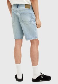 Ljus tvättad denimshorts, knälängd, med två bakfickor och en brun läderlapp vid midjan. Bärs med vita strumpor och svarta skor.