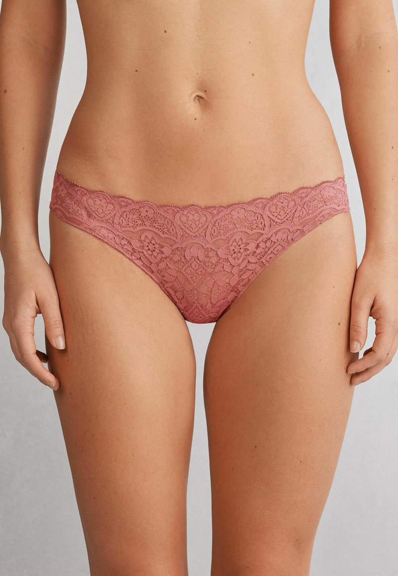 Lingerie en dentelle mauve, avec un motif floral délicat, une texture semi-transparente et une taille à bords festonnés pour une finition élégante.