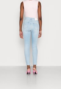 Jeans ajustados de color azul claro con una cintura alta, que cuentan con bolsillos traseros y una etiqueta blanca en la cintura. Combinados con sandalias de tacón rosas.