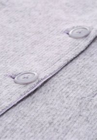 Ljusgrått tyg med en strukturerad yta, med två knappar i en ljuslila nyans och en sydd kant.