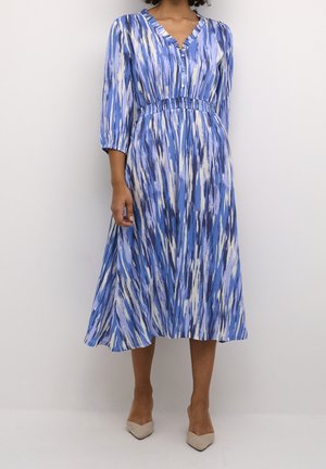 Blå mönstrad klänning med V-ringning, trekvartslånga ärmar och smockad midja. Har en flödande kjol och knappdetalj vid halsringningen.