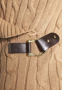 Beżowa dzianina w klasyczny wzór z prążkowanymi brzegami, z ciemnobrązowym skórzanym paskiem i złotą klamrą jako detalem.
