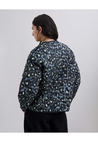 Chaqueta acolchada con una base negra y un patrón de leopardo en azul y crema. Hombros redondeados y un corte relajado.