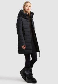 Black puffer coat, knee-length with large hood, horizontal stitching, side pockets, paired with black, insulated waterproof boots.