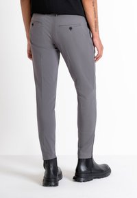 Pantalones ajustados gris de tejido suave, con dos bolsillos traseros, costuras laterales discretas, combinados con botas negras hasta el tobillo.