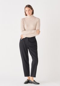 Beige coltrui, zwarte gepaste broek en zwarte loafers met een gouden kettingaccent. Zachte textuur en minimalistisch ontwerp.