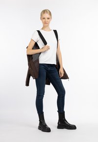 Brun pufferjakke med grå detaljer, båret åbenstående over en hvid t-shirt. Slim fit blå jeans og sorte gummistøvler til anklerne fuldender outfittet.