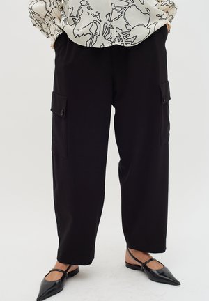 Black cargo pants with a relaxed fit, featuring two side pockets, and a smooth texture. Paired with pointy black flats.