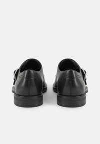 Chaussures en cuir noir avec une texture lisse, bout rond, petit talon et accent de boucle sur le côté ; présente un minimum de détails de couture.