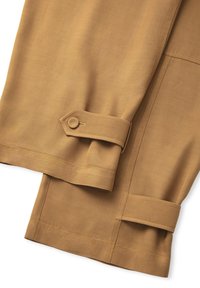 Khaki-colored trousers made of smooth fabric, featuring a fold with a button closure at the hem and visible stitching details.