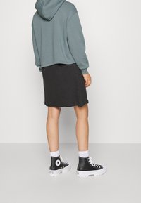 Sudadera corta color azul claro, falda de mezclilla negra con dobladillo deshilachado y zapatillas altas negras con suelas blancas y logo en el lateral.