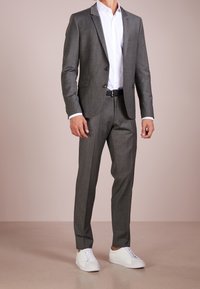 Completo grigio su misura con rever a punta, due bottoni e tessuto texturizzato, abbinato a una camicia bianca e sneaker bianche.