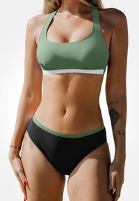 Grüner Sport-Bikini mit einem Hochkragen-Oberteil mit weißem Band und hochgeschnittenen schwarzen Bottoms mit grünem Akzent. Glattes, elastisches Material.