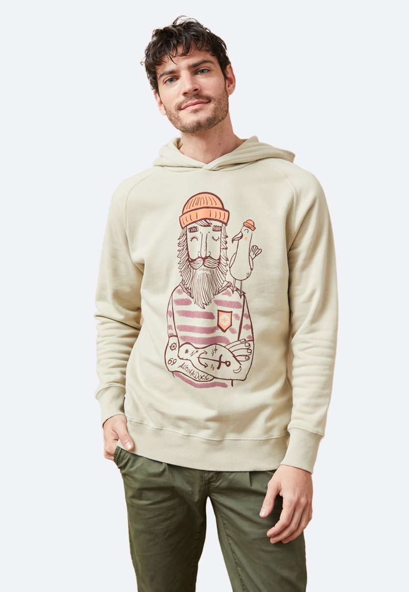 Sudadera beige de tela suave con un gráfico frontal de un hombre barbudo y un pájaro. Presenta una capucha con cordón y puños y dobladillo acanalados.