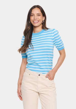 Haut en tricot rayé bleu et blanc avec des manches courtes à volants et un col rond, associé à un pantalon beige clair. Texture lisse, design décontracté.