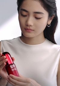 Bouteille en verre rouge avec un sommet arrondi, ornée de texte blanc ; tenue dans des mains. Fini lisse et brillant, présentée contre un fond doux et atténué.
