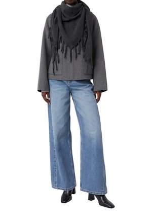 Grijze wolblend jas met brede mouwen, gecombineerd met lichtblauwe wijde jeans. De outfit isaccessoire met een donkergrijze fringed sjaal.
