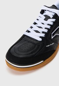 Baskets en cuir noir avec lacets blancs, semelle en caoutchouc couleur gomme, détails perforés et logo discret sur le côté. Design de bout arrondi.
